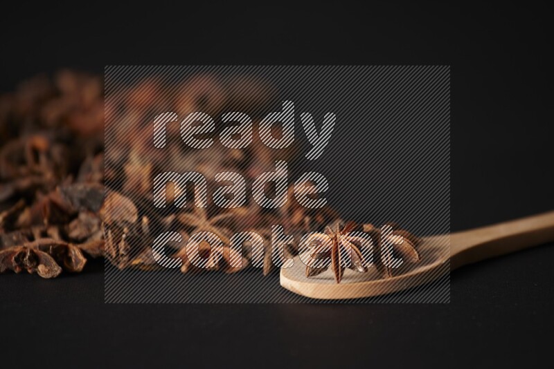 اليانسون النجمي في ملعقة خشبية ومتناثر على أرضية سوداء