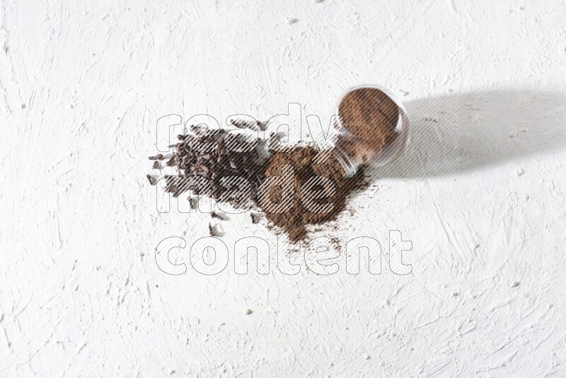 A glass spice jar full of cloves powder flipped and powder came out of it with cloves spread on textured white flooring