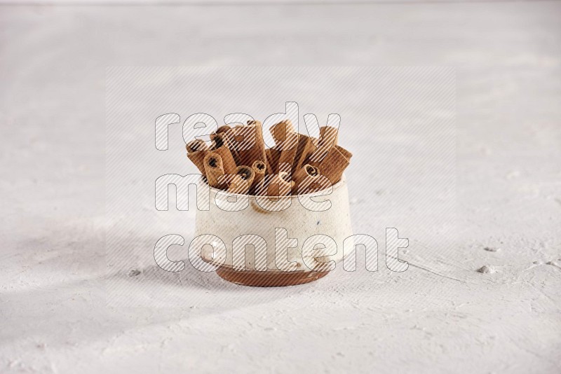 Cinnamon sticks in a beige bowl and more sticks beside it on white background