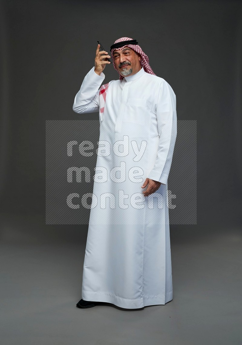 Saudi man with shomag Standing talking on phone on gray background