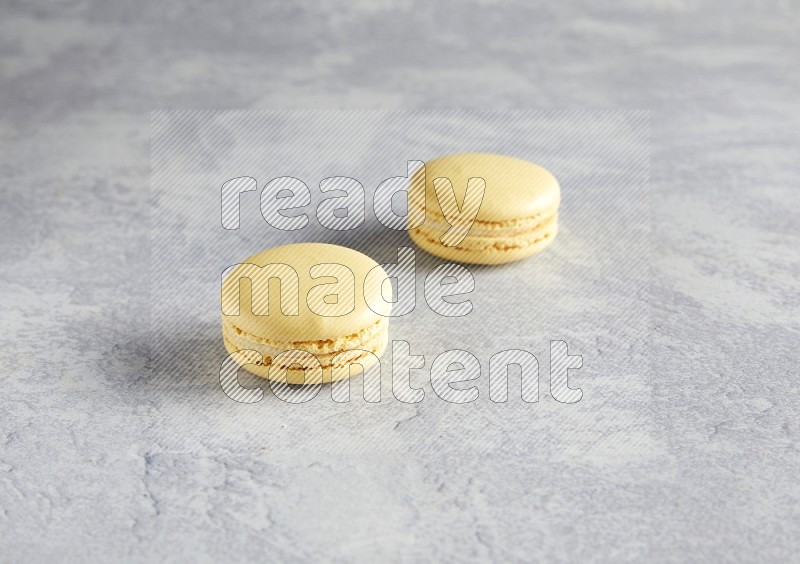 45º Shot of two Yellow Vanilla macarons  on white  marble background