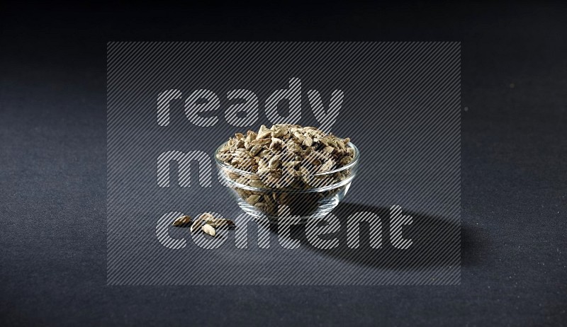 وعاء زجاجي ممتلئ بحبوب الهيل ومزيد من الحبوب متناثرة تحت الوعاء على خلفية سوداء