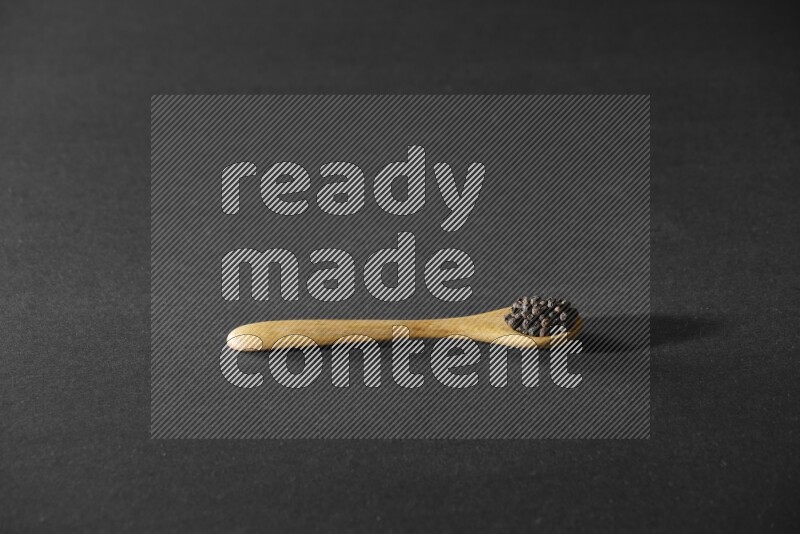 حبوب الفلفل الأسود في ملعقة خشبية علي خلفية سوداء