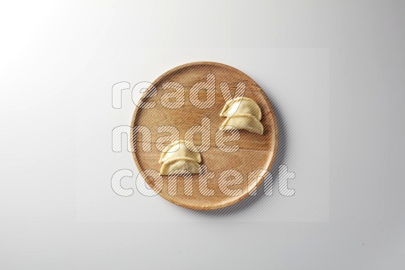 Four Sambosas on a wooden round plate on a white background