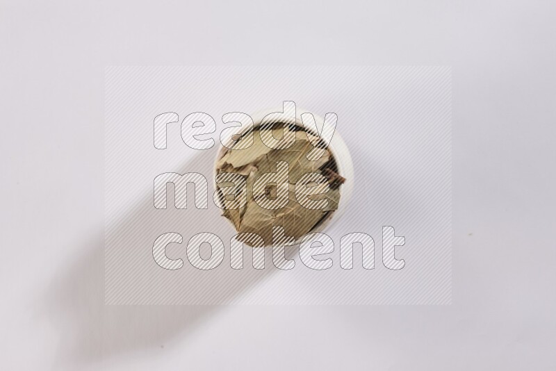 A beige pottery bowl full of dried bay leaves on white flooring