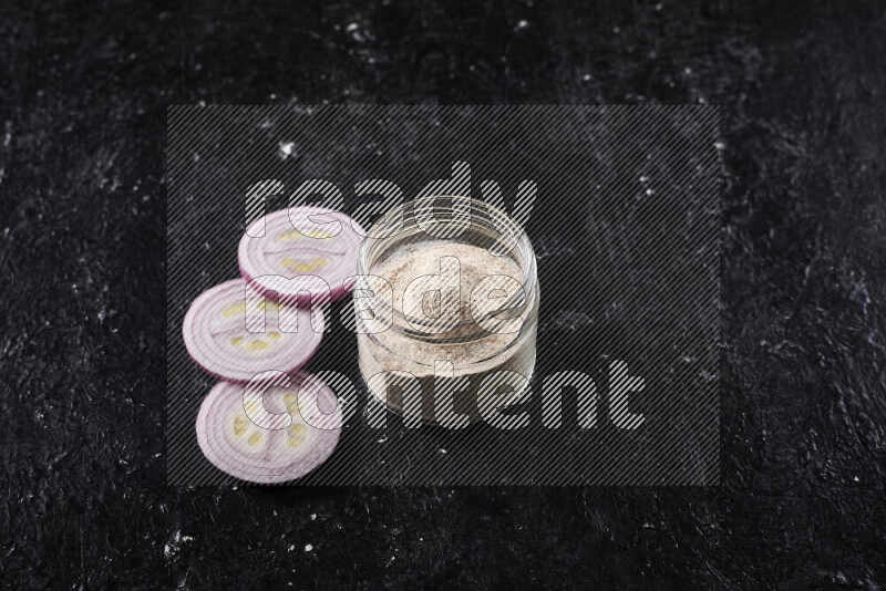 A glass jar full of onion powder on black background