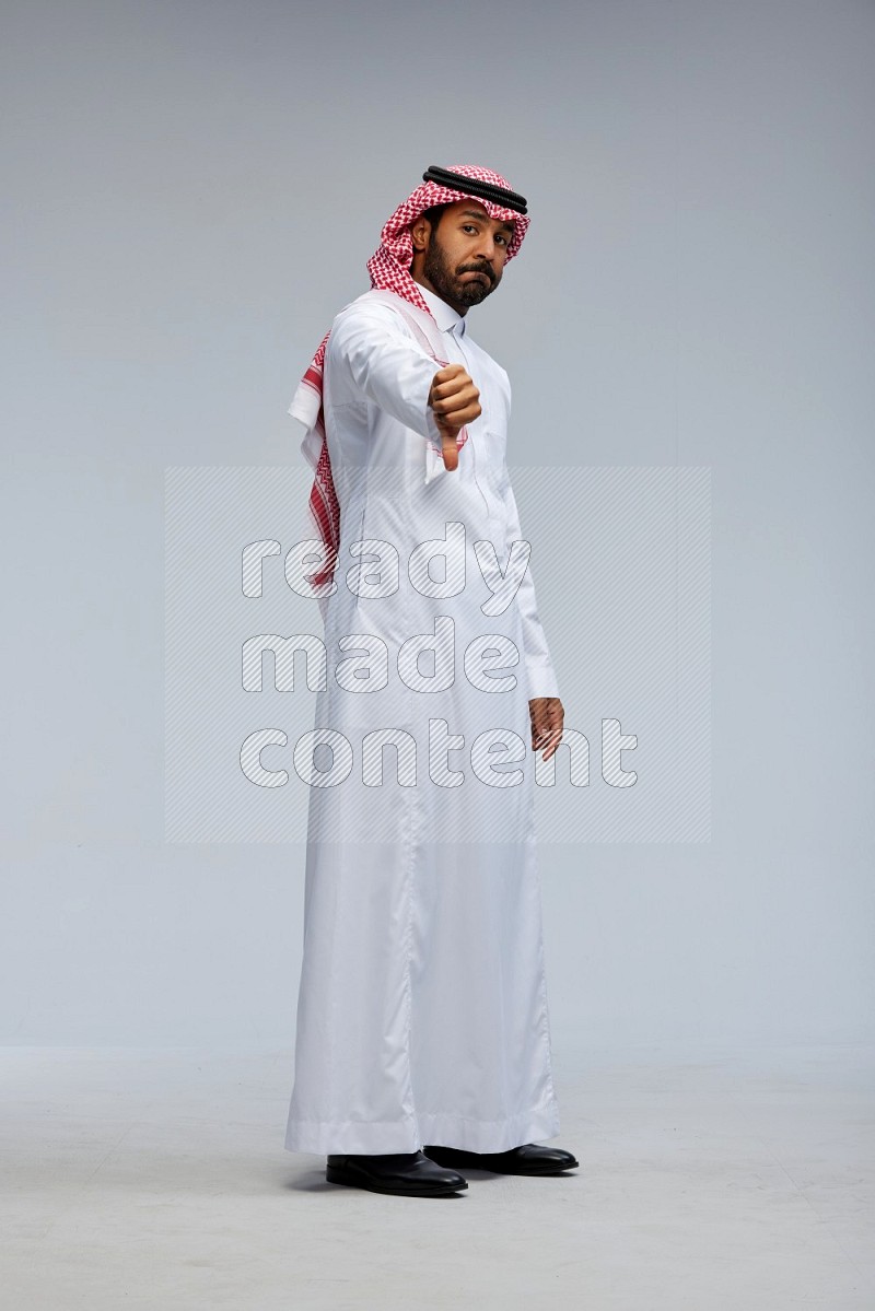 Saudi man Wearing Thob and shomag standing interacting with the camera on Gray background