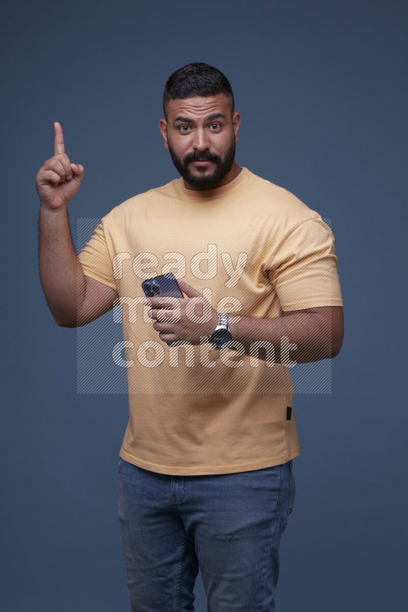 A man Pointing at a Smartphone on Blue Background wearing Orange T-shirt