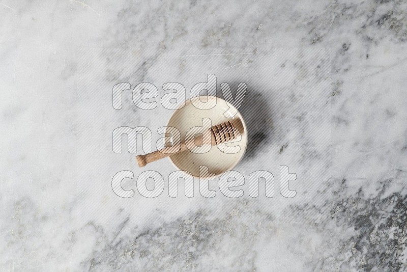 Beige Pottery Bowl with wooden honey handle in it, on grey marble flooring, Top View