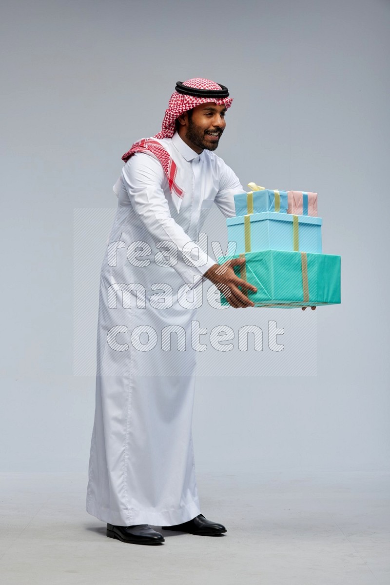 Saudi man Wearing Thob and shomag standing holding gift box on Gray background