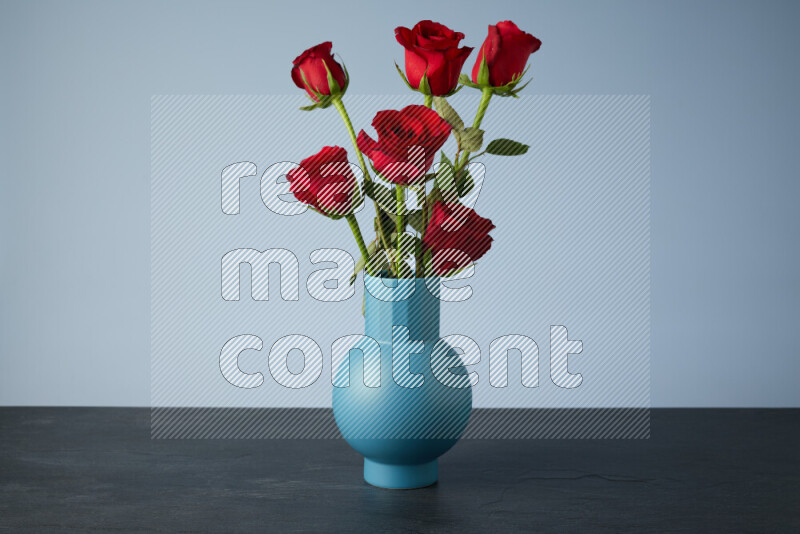 An arrangement of vivid red roses in a blue vase on black marble background