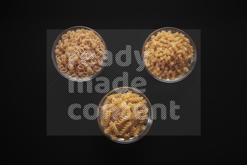 Different pasta types in glass bowls on black background