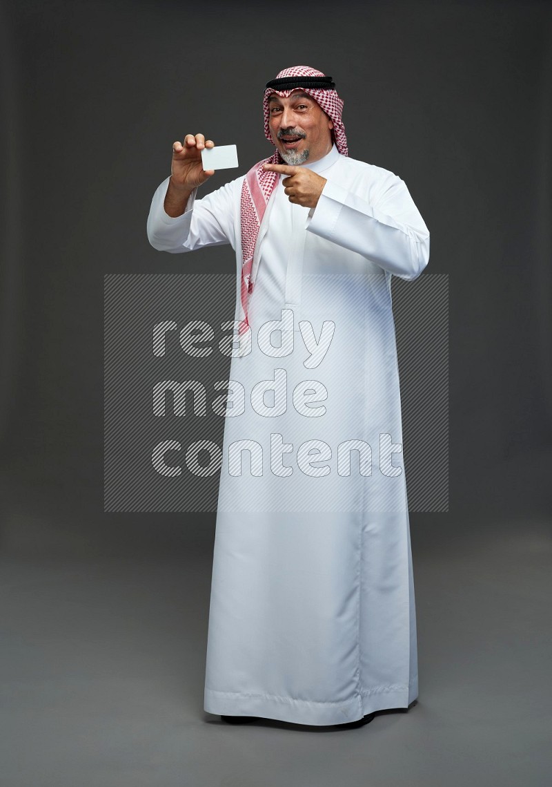 Saudi man with shomag Standing holding ATM card on gray background