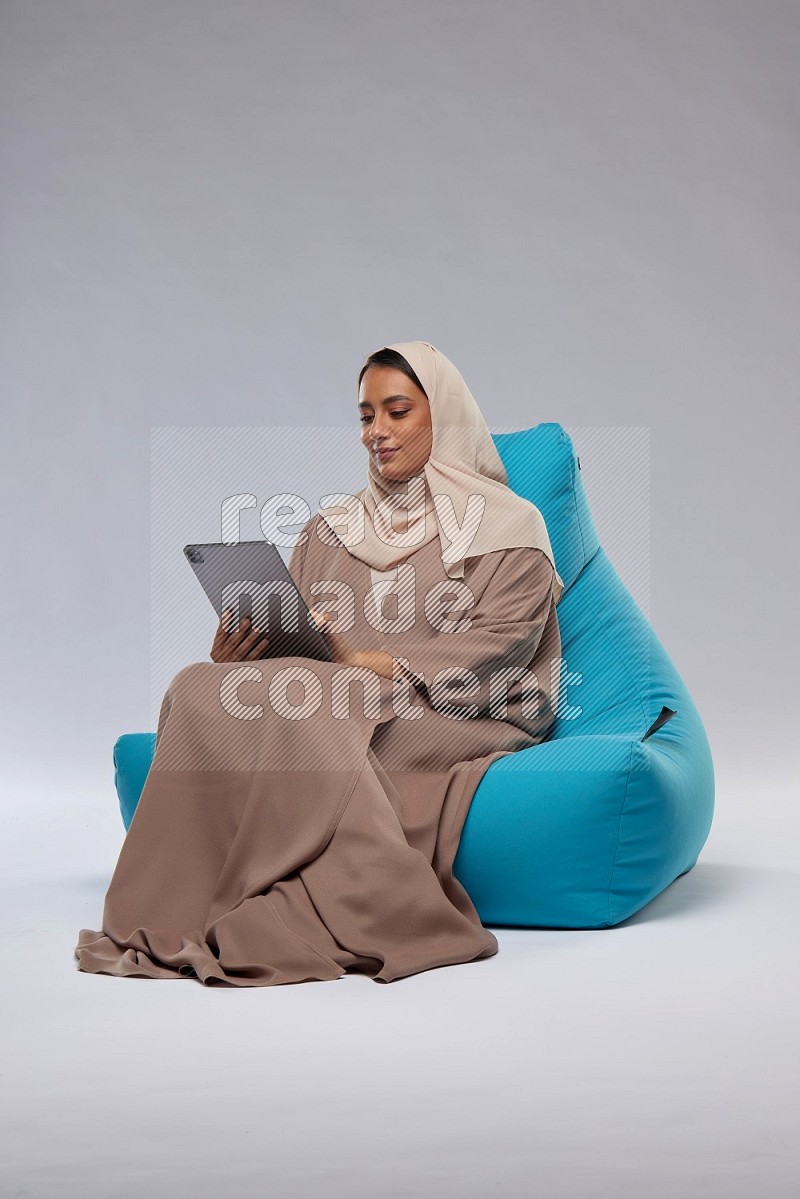 A Saudi woman sitting on a blue beanbag and working on tablet