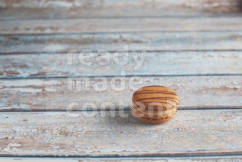 45º Shot of light brown Almond Cream macaron on light blue wooden background