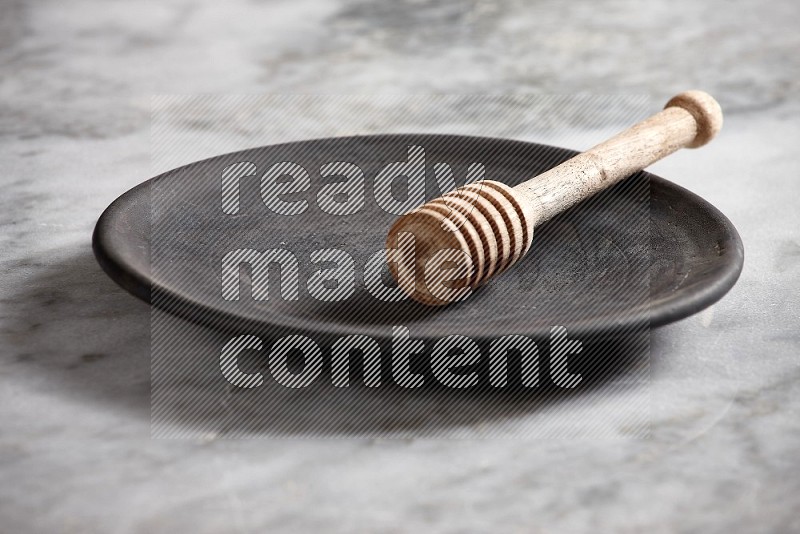 Black Pottery Plate with wooden honey handle in it, on grey marble flooring, 15 degree angle