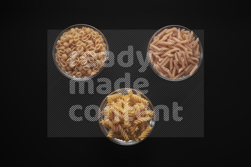 Different pasta types in glass bowls on black background