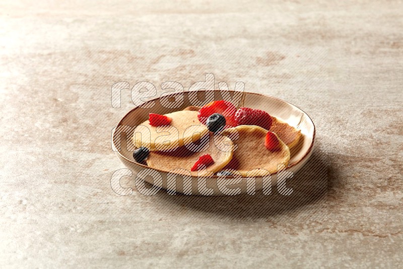 Five stacked mixed berries mini pancakes in an irregular plate on beige background