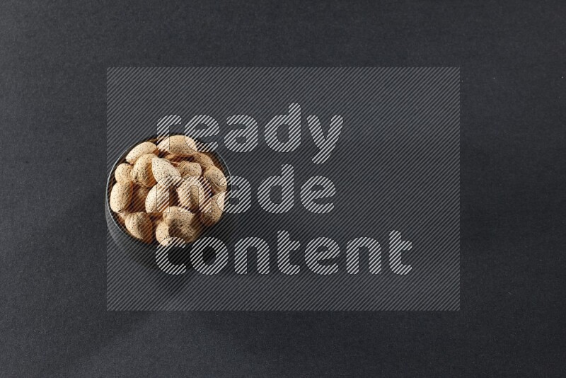 A black pottery bowl full of almonds on a black background in different angles
