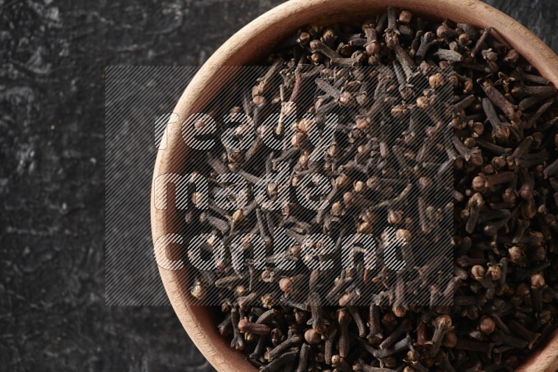 A wooden bowl full of cloves on a black flooring