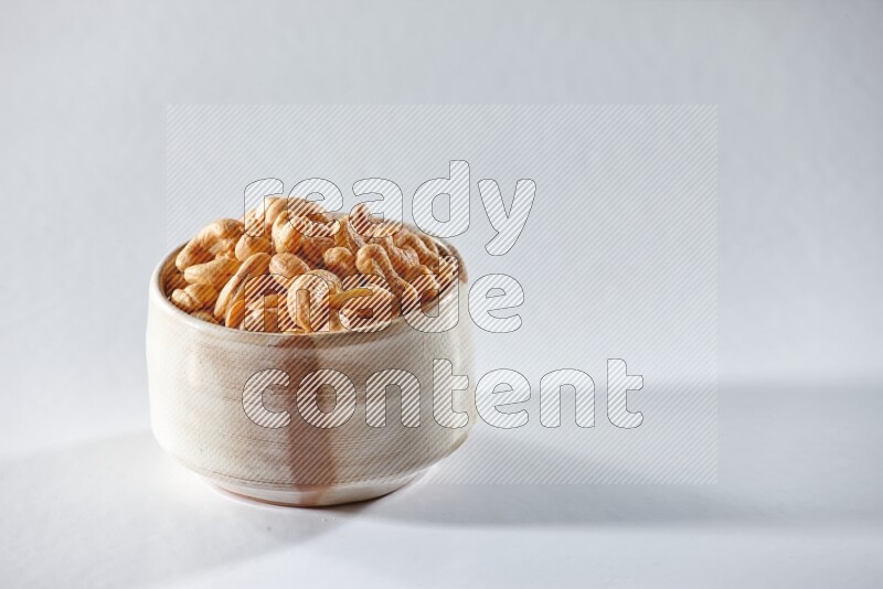 A beige ceramic bowl full of cashews on a white background in different angles