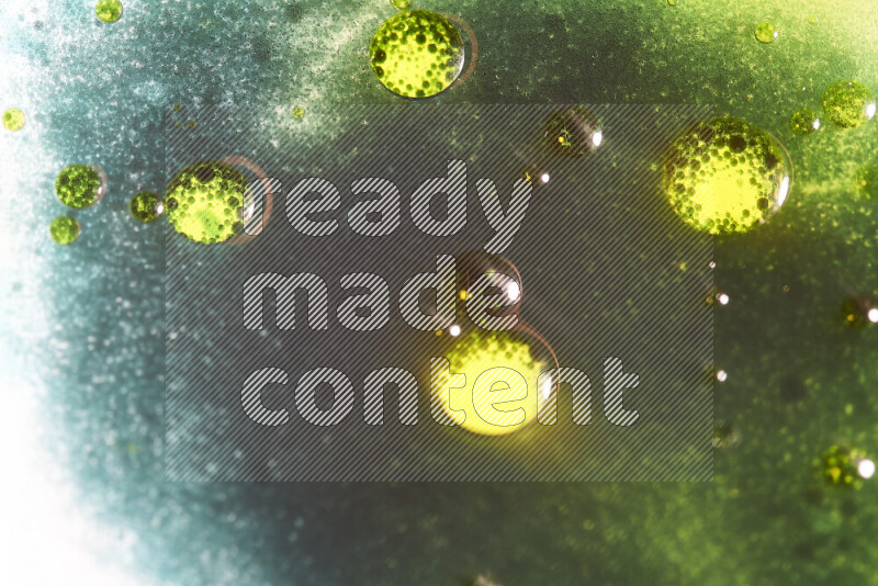 لقطات مقربة لقطرات ألوان مائية خضراء وصفراء على سطح الزيت على خلفية بيضاء