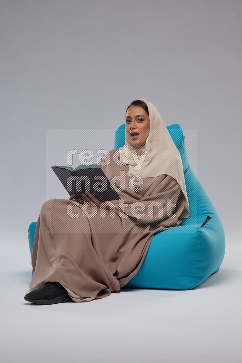 A woman sitting on a blue beanbag and reading a book