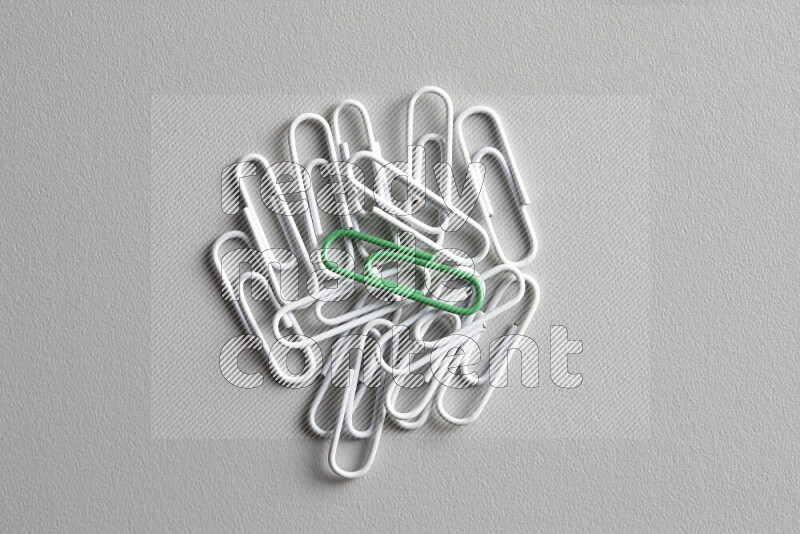 A green paperclip surrounded by bunch of white paperclips on grey background