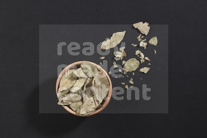 وعاء خشبي ممتلئ بأوراق الغار المجففة علي أرضية سوداء