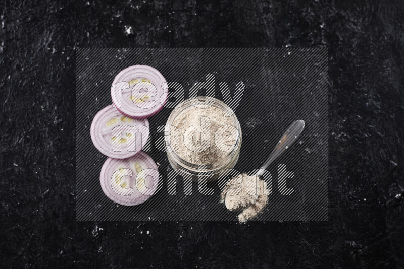 A glass jar full of onion powder on black background