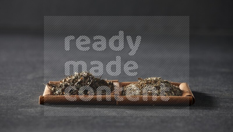 مربعان من أعواد القرفة ممتلئان بحبوب الكمون والريحان المجفف علي خلفية سوداء