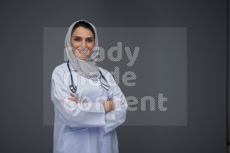 A female doctor wearing a light gray head scarf standing on grey background.