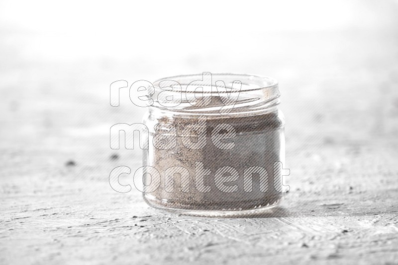 A glass jar full of black pepper powder on a textured white flooring