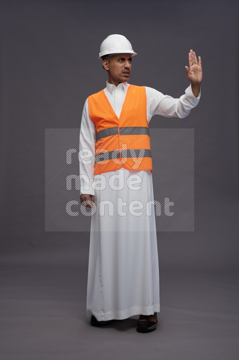 Saudi man wearing thob with engineer vest standing interacting with the camera on gray background