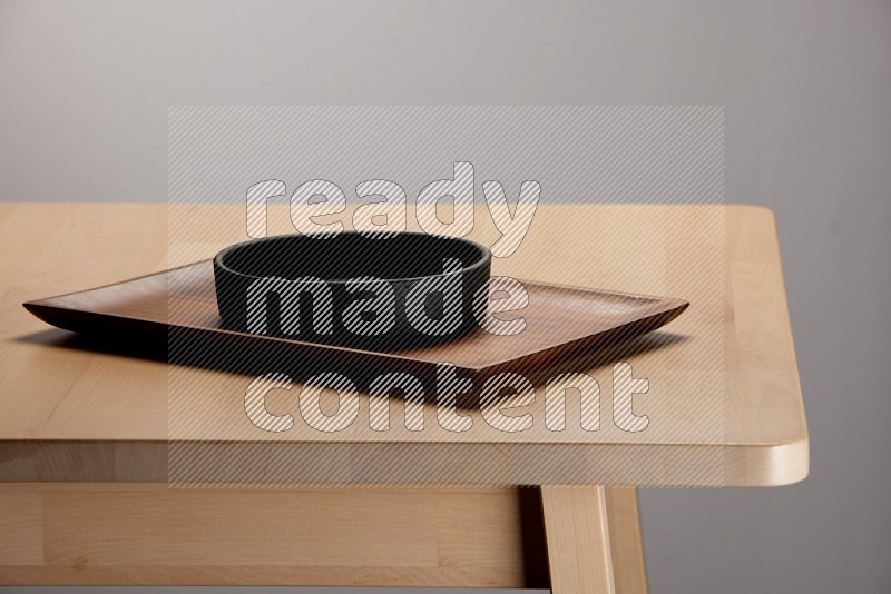 black bowl placed on a rectangular wooden tray on the edge of wooden table