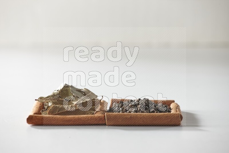 2 squares of cinnamon sticks full of black peppers and bay laurel leaves on white flooring