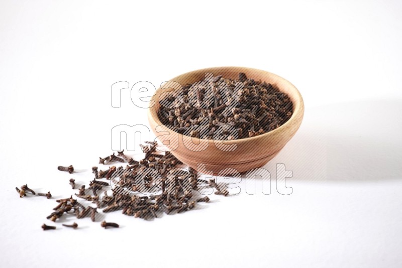 A wooden bowl full of cloves with spread grains on a white flooring