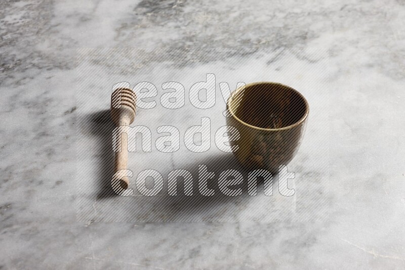 Multicolored pottery cup with wooden honey dipper on the side on grey marble background