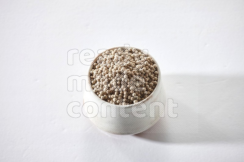 A beige pottery bowl full of white pepper beads on white flooring