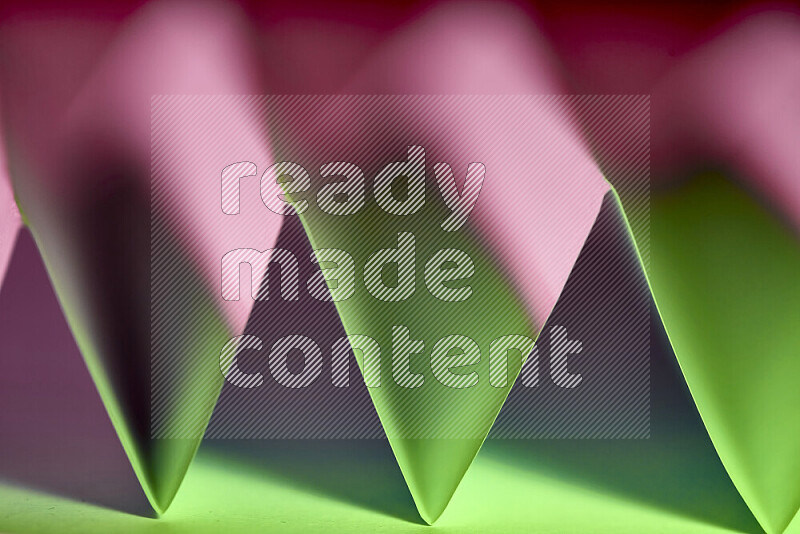 A close-up abstract image showing sharp geometric paper folds in green and purple gradients