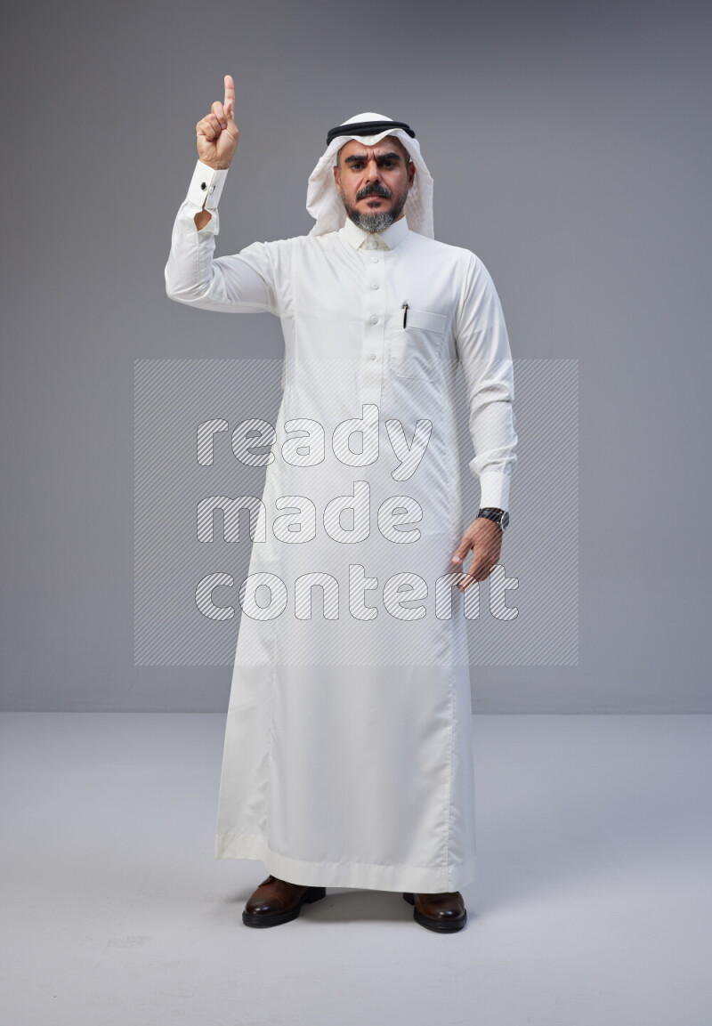 Saudi man Wearing Thob and white Shomag standing interacting with the camera on Gray background