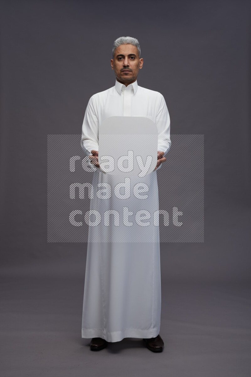 Saudi man wearing thob standing holding social media sign on gray background