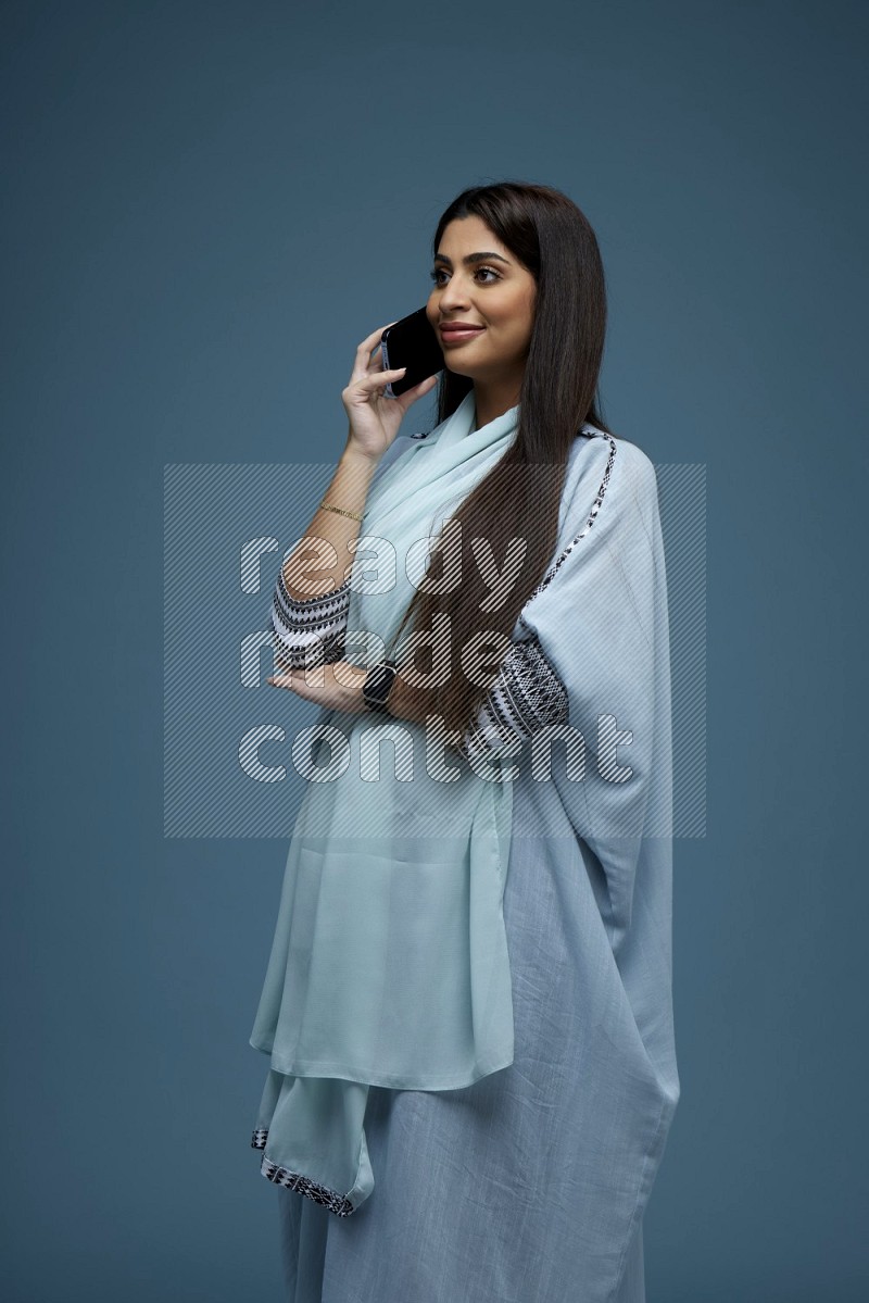 A Saudi woman having a Call in a blue background wearing a blue Abaya with no hijab