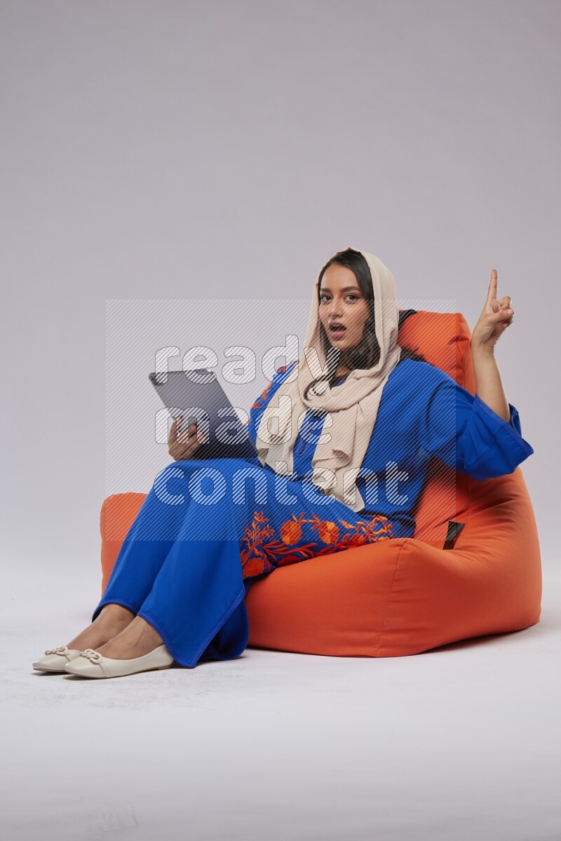 A Saudi woman sitting on an orange beanbag and working on tablet