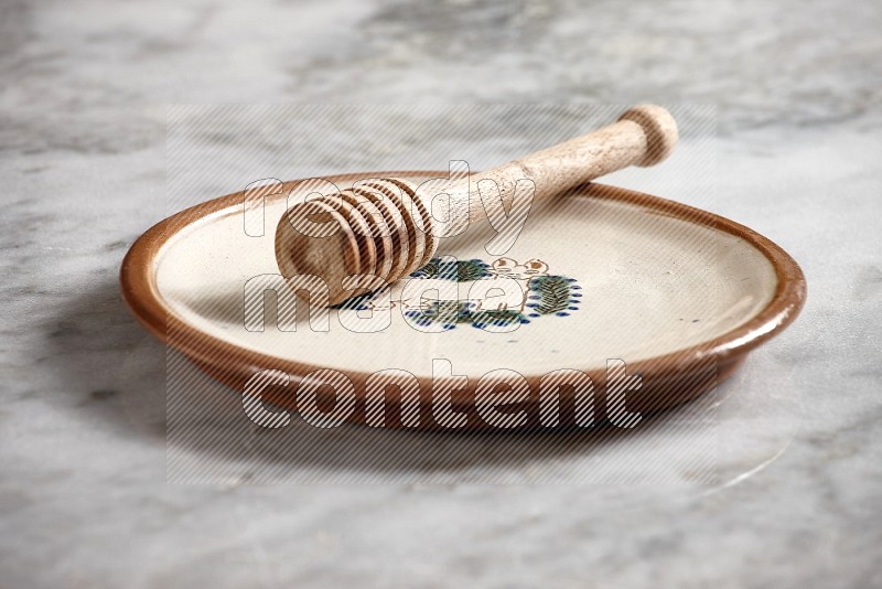 Decorative Pottery Plate with wooden honey handle in it, on grey marble flooring, 15 degree angle