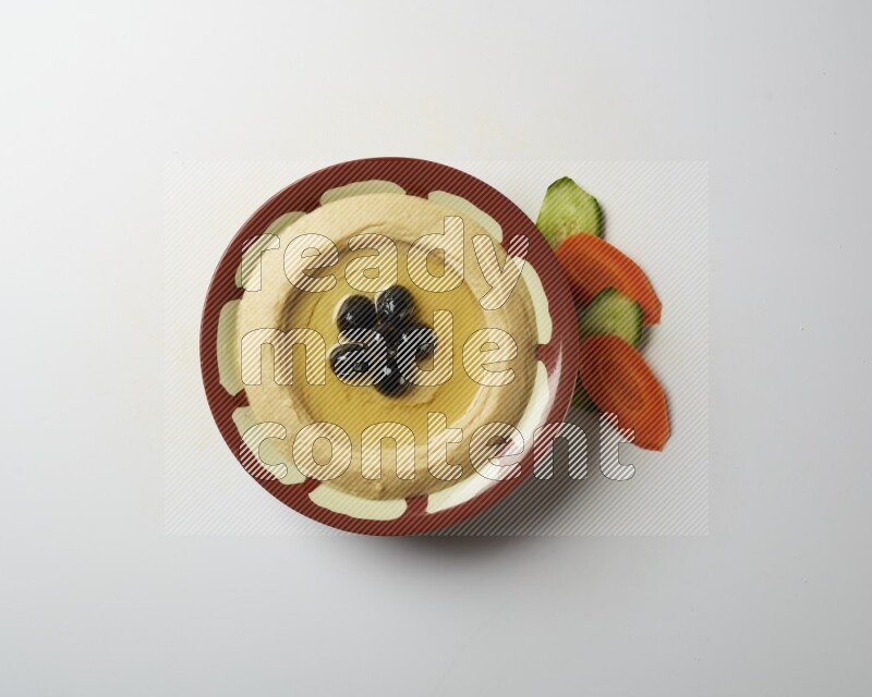 Hummus in a traditional plate garnished with black olives on a white background