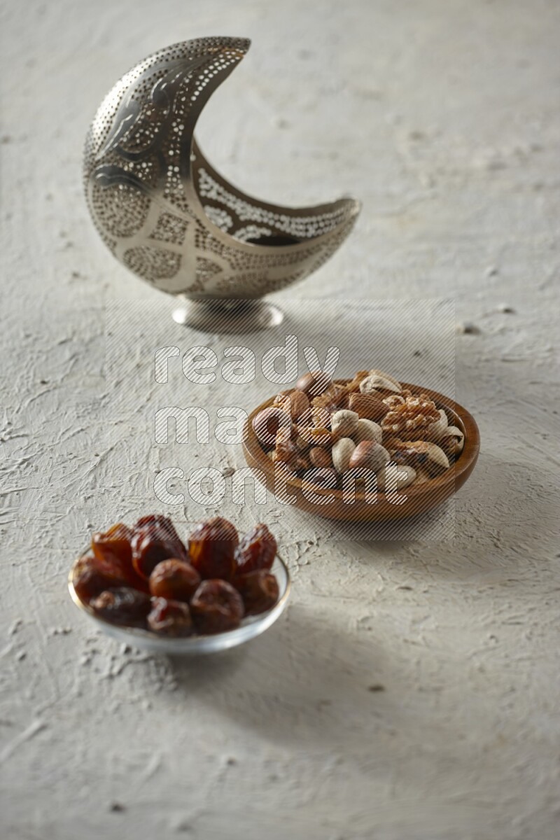A silver lantern with different drinks, dates, nuts, prayer beads and quran on textured white background