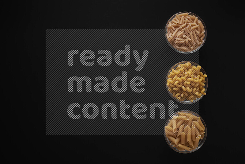 Different pasta types in 3 glass bowls on black background