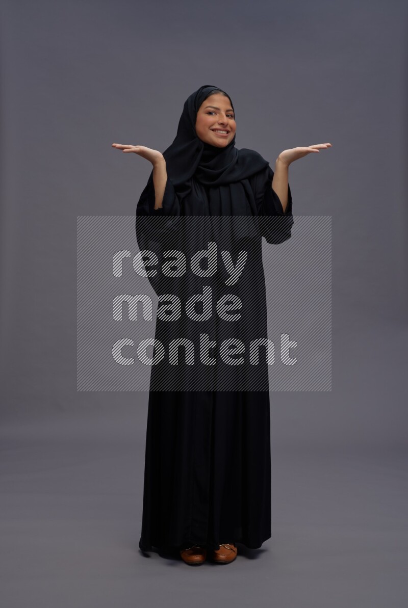 Saudi woman wearing Abaya standing interacting with the camera on gray background