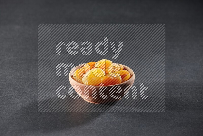 A wooden bowl full of dried apricots on a black background in different angles